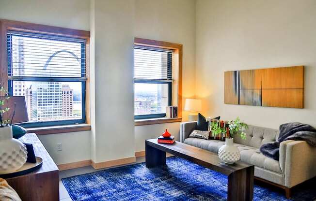 A living room with a grey couch, a blue rug, and a painting on the wall.