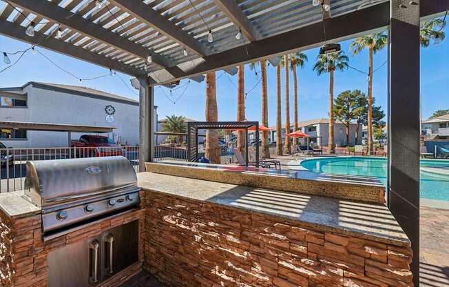 A patio with a grill and a pool in the background.