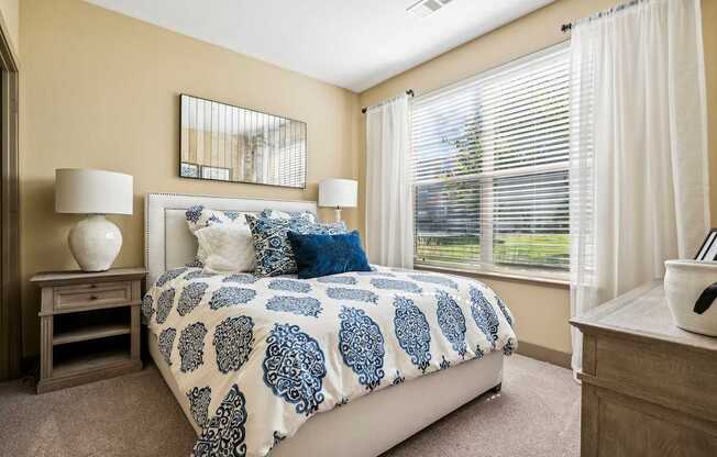 A bedroom with a bed, nightstands, and a window with blinds.