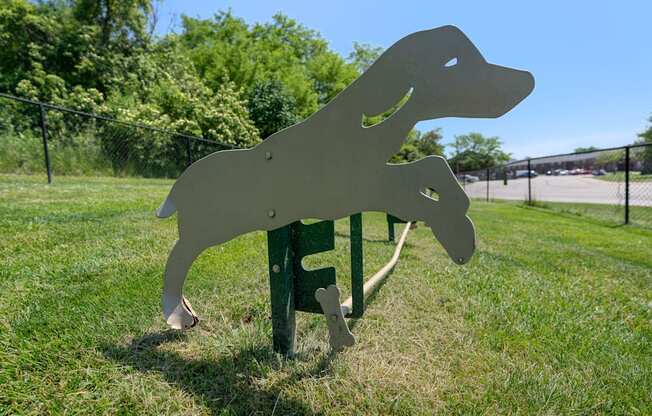 a metal dog statue in the grass near a fence