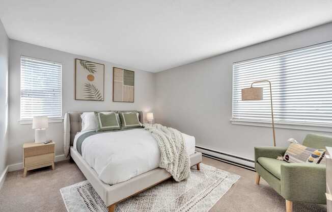 A bedroom with a large bed, a green chair, and two lamps.