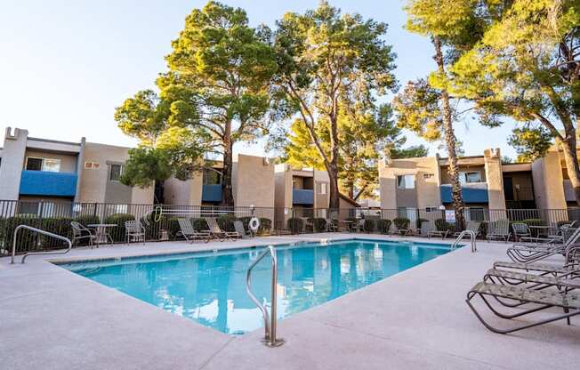 A swimming pool surrounded by trees and chairs in front of a building.