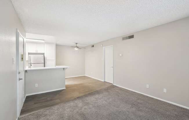 an empty living room and kitchen with white walls and wood flooring