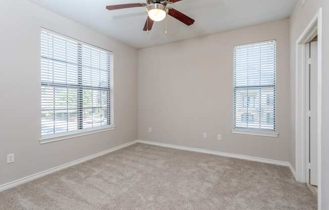 an empty bedroom with a ceiling fan and two windows