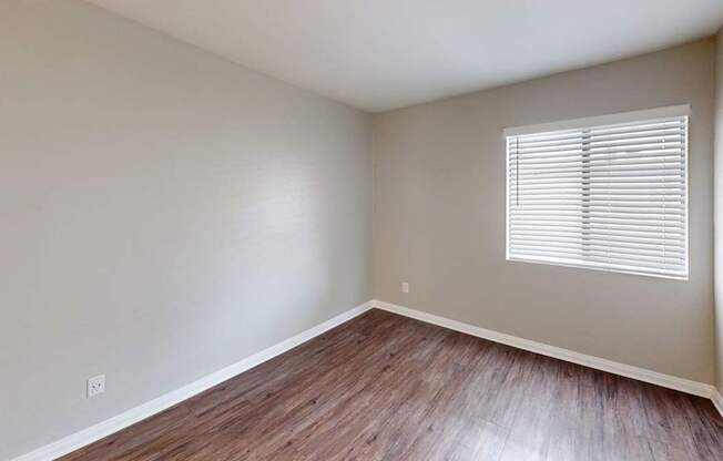 A room with wooden flooring and a window with blinds.