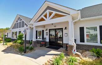 The front of the grey and white clubhouse with green plants and rocking chairs on the porch.
