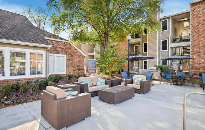 A patio with a couch, chairs, and a table with a tree in the background.