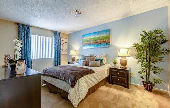 A bedroom with a bed, nightstand, and a potted plant.