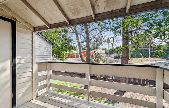 A balcony with a wooden railing and a view of a tree and a fence.