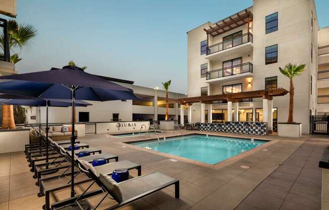 A pool area with sun loungers and umbrellas in front of a building.