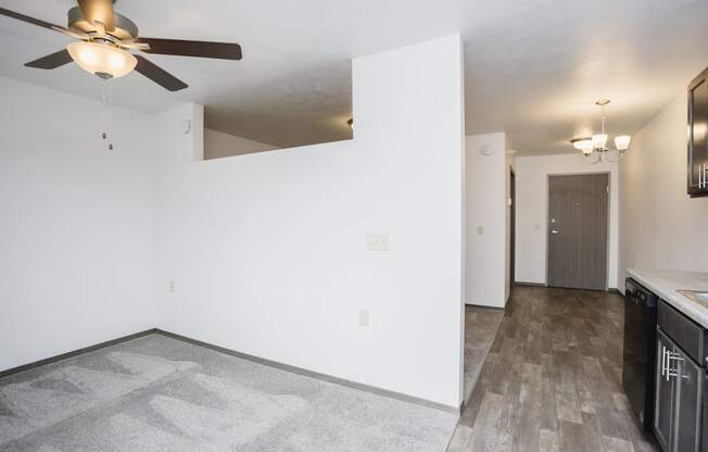 an empty living room with a ceiling fan and a kitchen