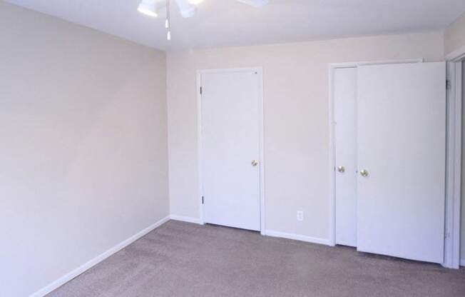 Bedroom with two closets, white walls, and grey carpet.