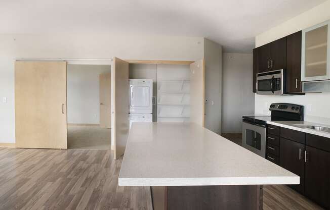 a kitchen with white granite countertops, grey hardwood floors and dark colored kitchen cabinets