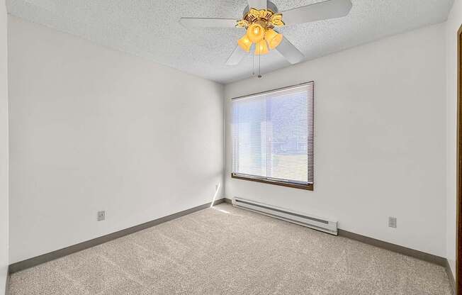 A room with a ceiling fan and a window with blinds.