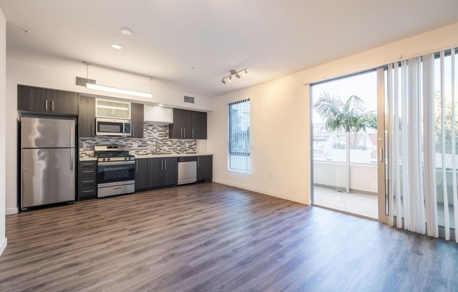 an empty living room with a kitchen and sliding glass doors