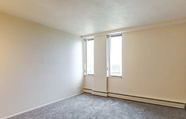 A room with a grey carpet and two windows.