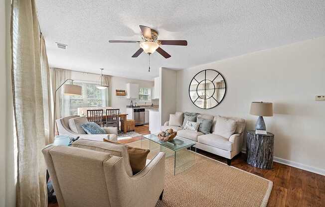 A living room with a beige couch, a glass coffee table, and a ceiling fan.