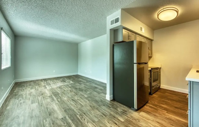 an empty living room with a refrigerator and a kitchen