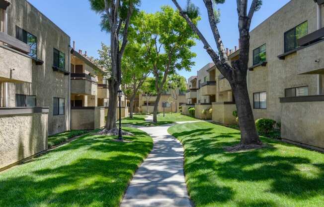 a sidewalk between two apartment buildings with green grass and trees