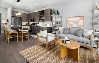 A modern living room with a grey couch, wooden coffee table, and a kitchen area in the background.