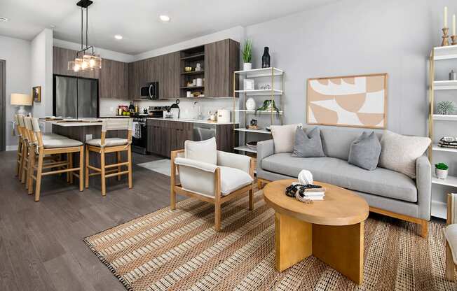 A modern living room with a grey couch, wooden coffee table, and a kitchen area in the background.