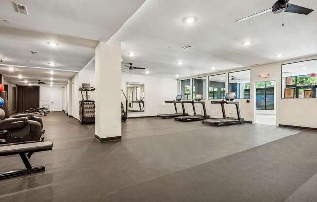 A spacious gym with treadmills, elliptical machines, and a ceiling fan.