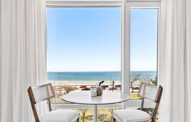 A dining table with chairs is set up by a window with a view of the beach.