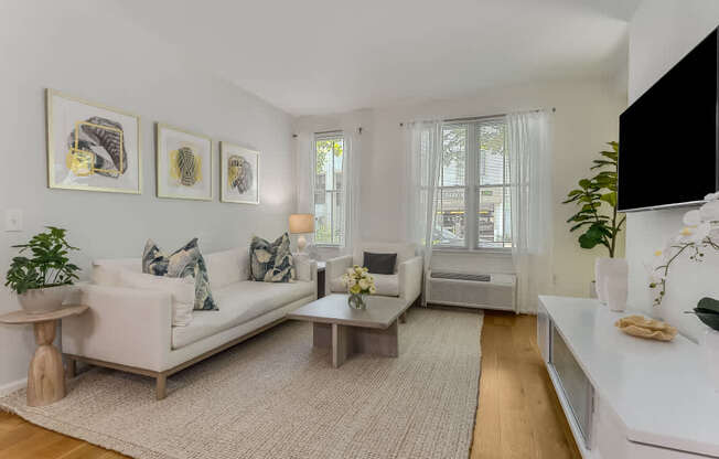A living room with a white couch, a coffee table, and a flat screen TV mounted on the wall.