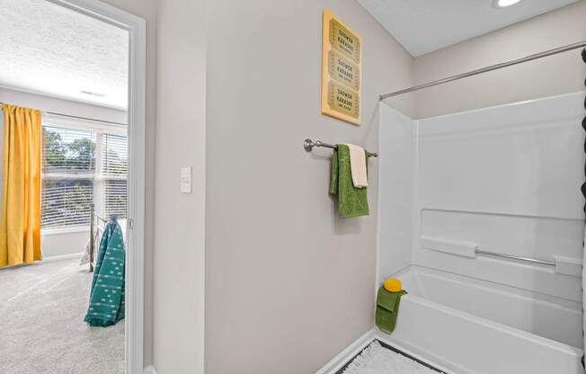 A bathroom with a white tub and a green towel hanging on the door.