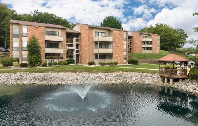 A fountain in the middle of a pond in front of apartment buildings.