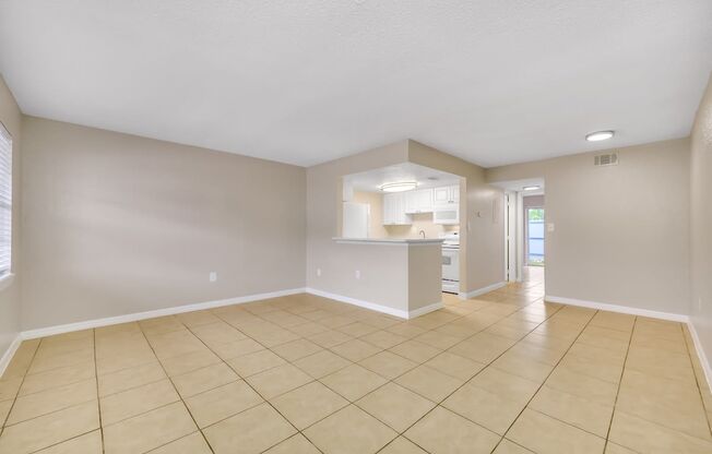 the spacious living room and kitchen of a home with tiled floors