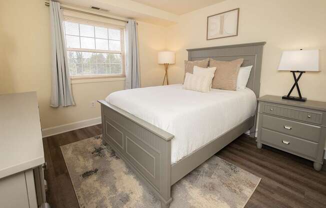 A bedroom with a large bed, a nightstand, and a window with curtains.