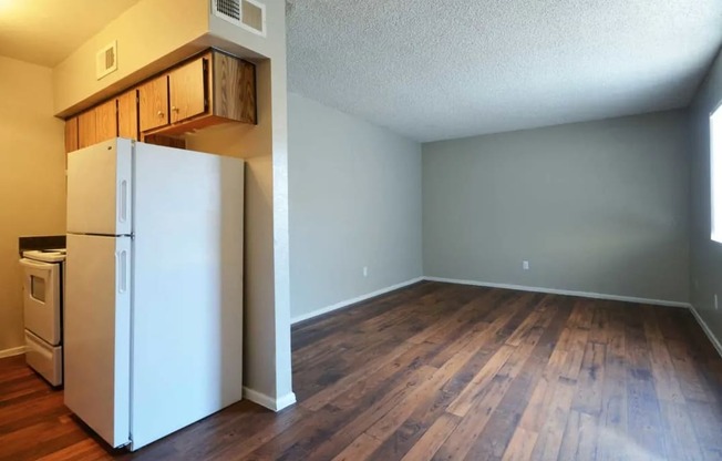 an empty living room with a refrigerator and wood floors