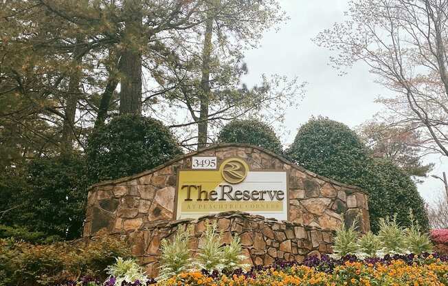 A sign for The Reserve surrounded by flowers and trees.