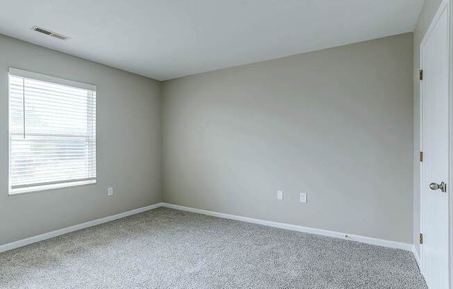 A room with a carpeted floor and a window with blinds.