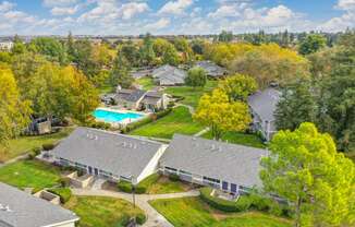 Elevated drone shot of the Pinecrest exterior community. Single story buildings with the blue swimming pool area in the distance. at Pinecrest Apartments, California