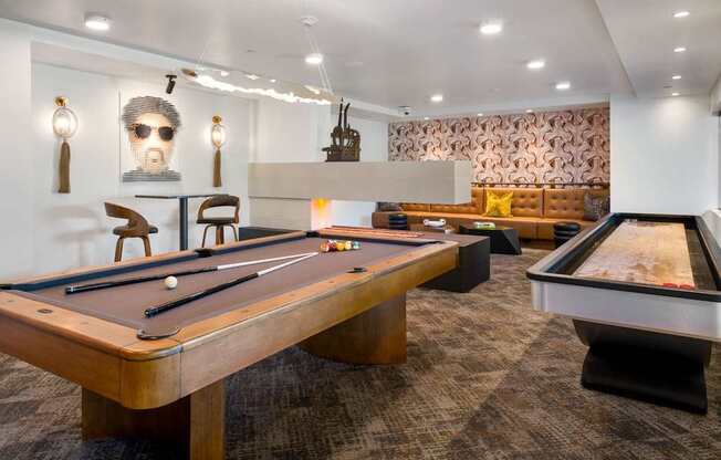 A pool table is in the middle of a room with a foosball table to the right.