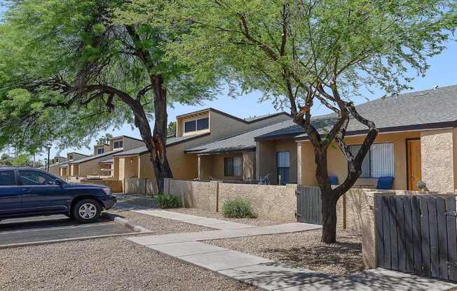 A blue car is parked on the street in front of a house with a tree in front of it.