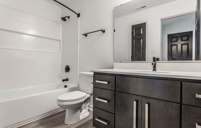 A white toilet sits in a bathroom with a wooden vanity and a large mirror.
