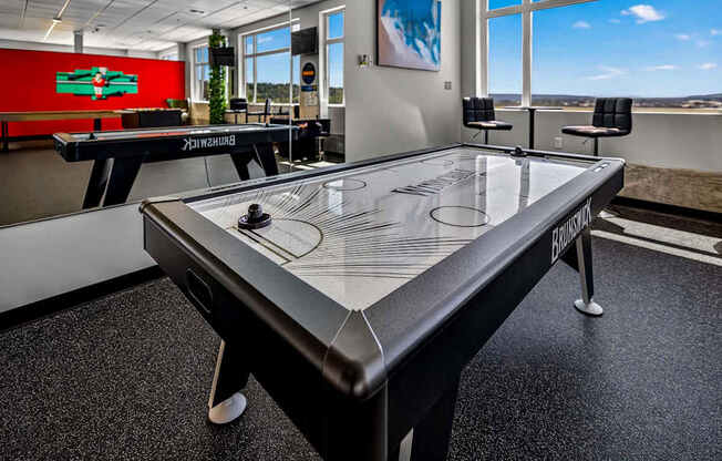 A black air hockey table in a room with a red wall and a window.