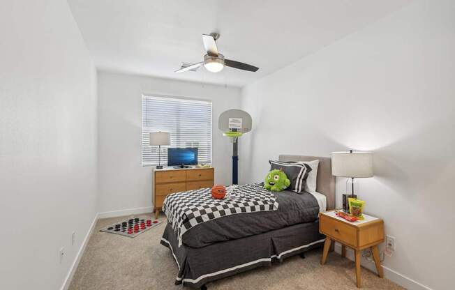 A bedroom with a bed, a ceiling fan, and a window with blinds.