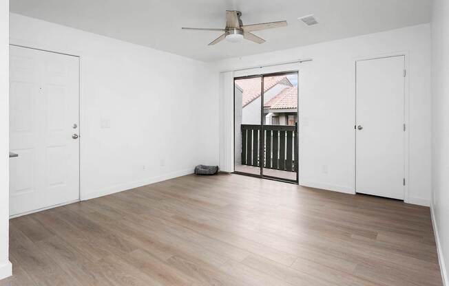 A room with a ceiling fan and a window with a view of a house.