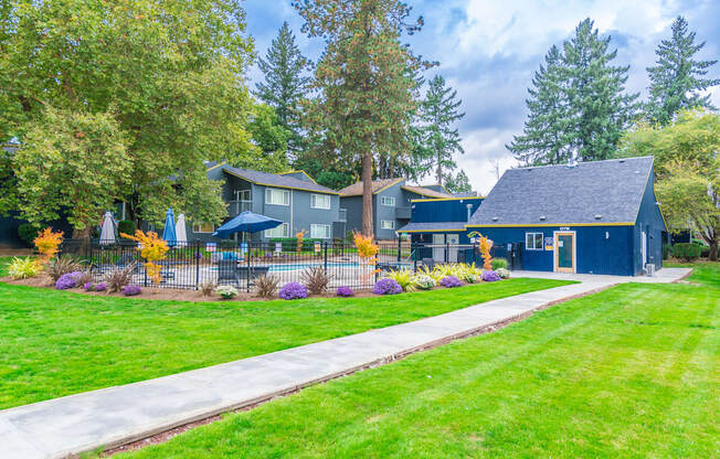 a sidewalk leading to a blue house with a pool in the front and trees in the background