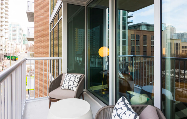 A balcony with brushed silver metal railings that fits two armchairs and a side table, with full-width floor-to-ceiling windows behind.