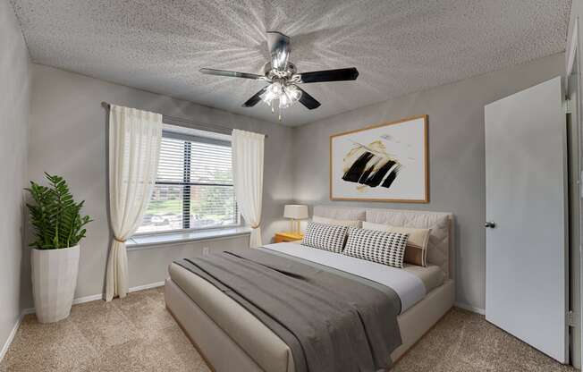 A bedroom with a bed, a ceiling fan, and a painting on the wall.