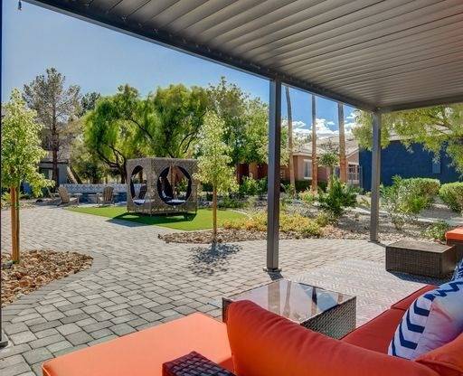 A patio with a couch and a table with a view of a garden and a building.