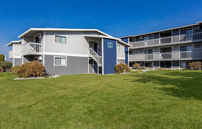 Exterior view of manicured grounds and building, and blue skies in the background at The Lakes Apartments, Moses Lake, WA.