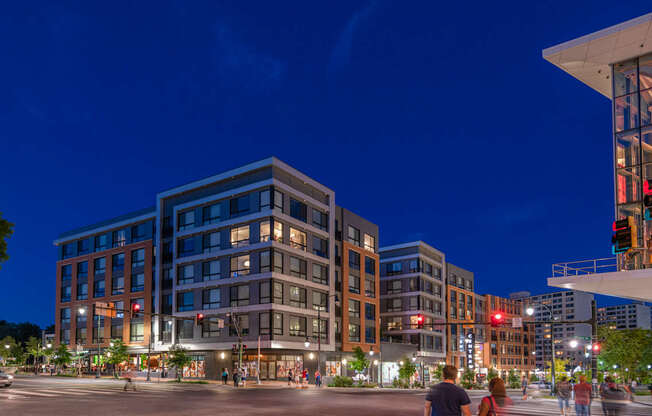 A city street at night with people walking and buildings with lit up windows.