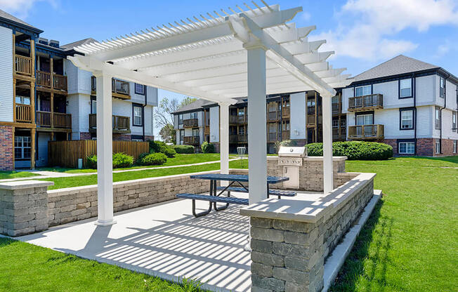 a pergola with a picnic table in front of an apartment complex