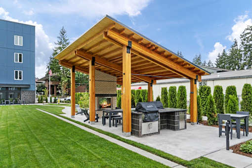 A wooden pergola with a grill and seating area in a backyard.